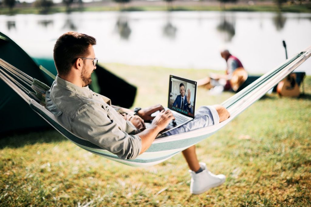remote work cybersecurity, a man working on a laptop while sitting on a hammock